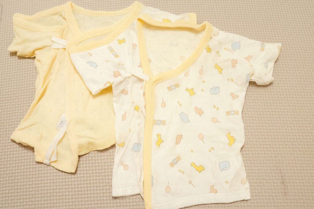 冬生まれの赤ちゃん向け短肌着とコンビ肌着の写真。やさしい黄色とベビー柄の肌着がベビー用品の出産準備として並べられている。